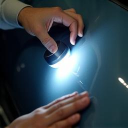 A detailer inspecting car paint with a specialized light.